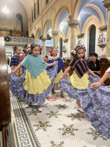 Young girls in traditional Ballet Folklorico dance costumes perform in the center aisle of St. Hedwig’s church