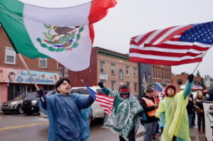 Daniel Mata, 18, left, waves a Mexican flag Tuesday, March 4 during a protest at Clark Park. Mata is a junior at Covenant High School Southwest. Photo by Dustin Blitchok/Planet Detroit