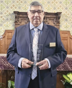 Vic in a recent photo, holding a trophy that is inscribed: Most Holy Trinity Parish • Sharing of the Green • 2025 • Corktown Detroit