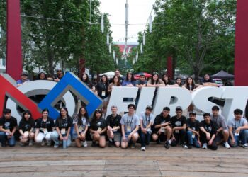 Team photo of all participants surrounding the FIRST Logo outside the main entrance to the competition