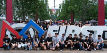 Team photo of all participants surrounding the FIRST Logo outside the main entrance to the competition