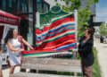 Two women unveiling a green Michigan Historic Site marker reading "Dra. Lucile Gajec" by pulling away a red, green, and blue striped serape, with a young boy watching beside them.