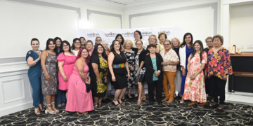 Large group of about 25 women posing together in a banquet room in front of a "MANA de Metro Detroit" banner.