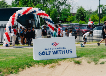 The entrance to Bank of America's Golf With Us event features a large red, white, and blue balloon arch above the event sign, with a white shuttle bus and event staff greeting young participants arriving for the program