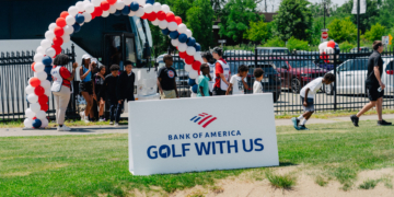 The entrance to Bank of America's Golf With Us event features a large red, white, and blue balloon arch above the event sign, with a white shuttle bus and event staff greeting young participants arriving for the program