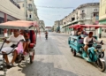 Motorized tricycle taxis carrying passengers pass each other on a wide Havana street lined with weathered colonial-style buildings.