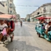 Motorized tricycle taxis carrying passengers pass each other on a wide Havana street lined with weathered colonial-style buildings.