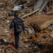 Emergency responder wearing a helmet and backpack walking across a large field of debris and rubble.