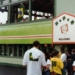 Exterior of a pub decorated with a Brazilian flag and a "Welcome" banner, with a crowd of soccer fans gathered outside and visible through an upstairs window.