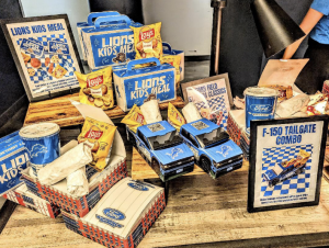 Detroit Lions branded merchandise and kids meal display featuring blue and gold Lions boxes, Lay's chips bags, toy Ford F-150 trucks, napkins, and promotional signage for Lions Kids Meal and Ford products.