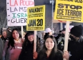 Nighttime protest scene with participants holding signs, including messages in Spanish about police abolition and signs reading "WALKOUT! NATIONWIDE SHUTDOWN JAN 20" and "FROM DETROIT TO MINNEAPOLIS STOP ICE TERROR." Participants bundled in winter clothing.