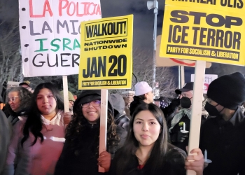 Nighttime protest scene with participants holding signs, including messages in Spanish about police abolition and signs reading "WALKOUT! NATIONWIDE SHUTDOWN JAN 20" and "FROM DETROIT TO MINNEAPOLIS STOP ICE TERROR." Participants bundled in winter clothing.