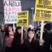 Nighttime protest scene with participants holding signs, including messages in Spanish about police abolition and signs reading "WALKOUT! NATIONWIDE SHUTDOWN JAN 20" and "FROM DETROIT TO MINNEAPOLIS STOP ICE TERROR." Participants bundled in winter clothing.