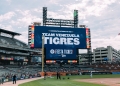 Wide view of Comerica Park stadium with a large digital scoreboard displaying "Congratulations to our TEAM VENEZUELA TIGRES" and "FIESTA TIGRES!" Decorative tiger statues sit atop the scoreboard structure, with Detroit skyline visible in background