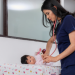 Healthcare worker in dark navy scrubs examining or providing care to an infant on a medical examination table in a clinical setting.